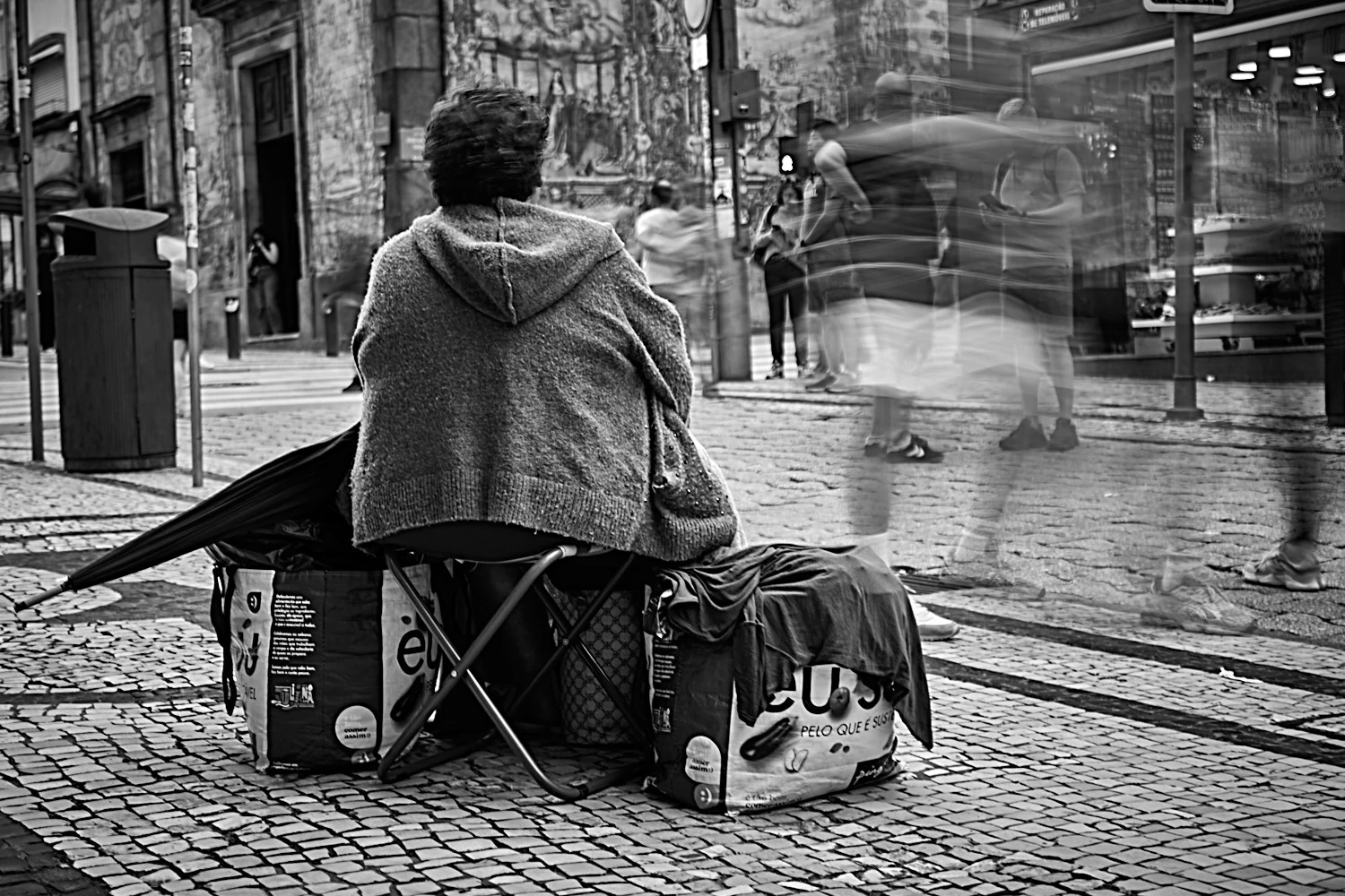 Sitting woman calling for attention, but everyone is passing by, in Porto