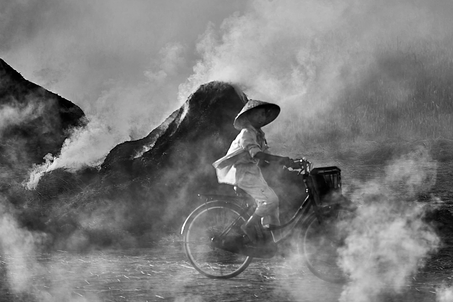 Child cycling through the smoke of burning straw in Vietnam